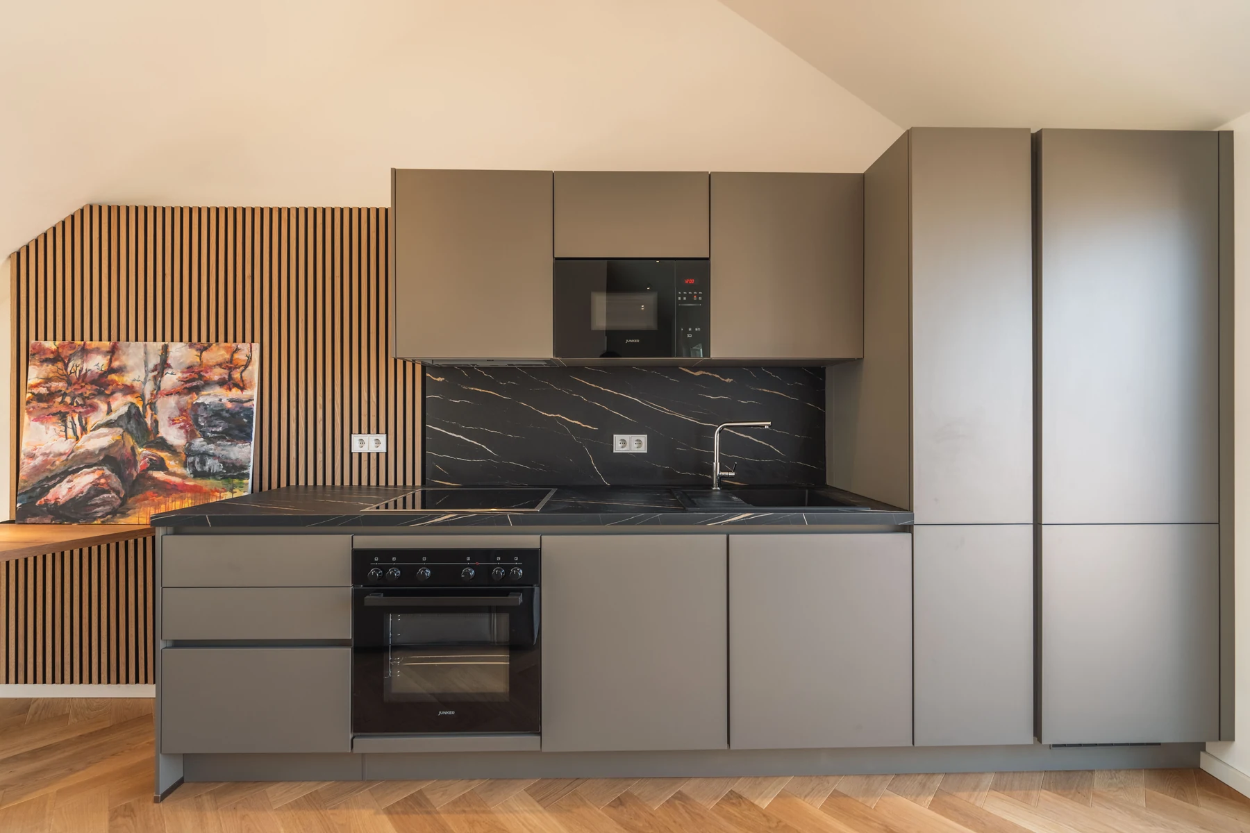 Küche mit dunklen Fronten, schwarzer Arbeitsplatte und Holzlamellenwand – Schellingstraße 32, München-Schwabing