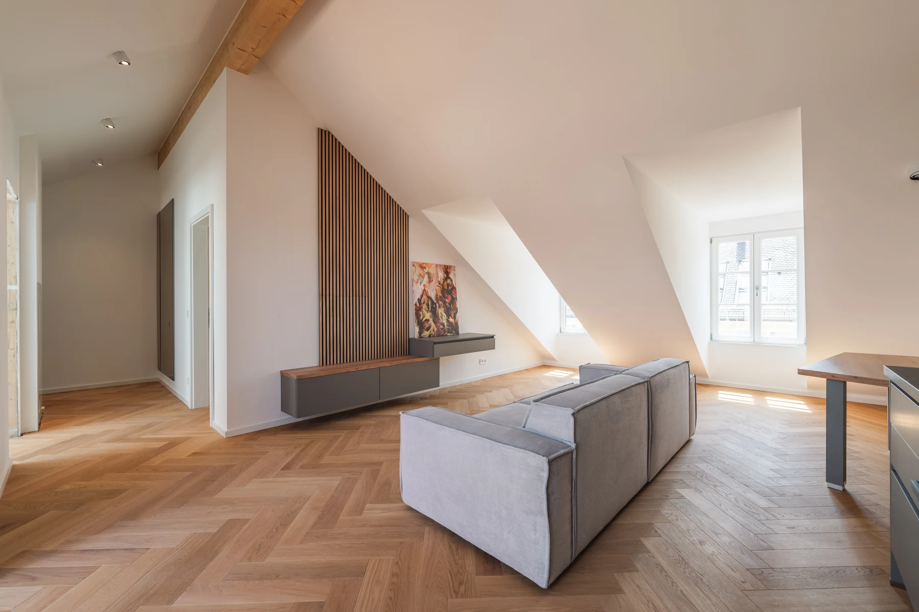 Wohnraum mit Gaubenfenstern, Holzlamellen, Sofa und Fischgrätparkett – Schellingstraße 32, München-Schwabing